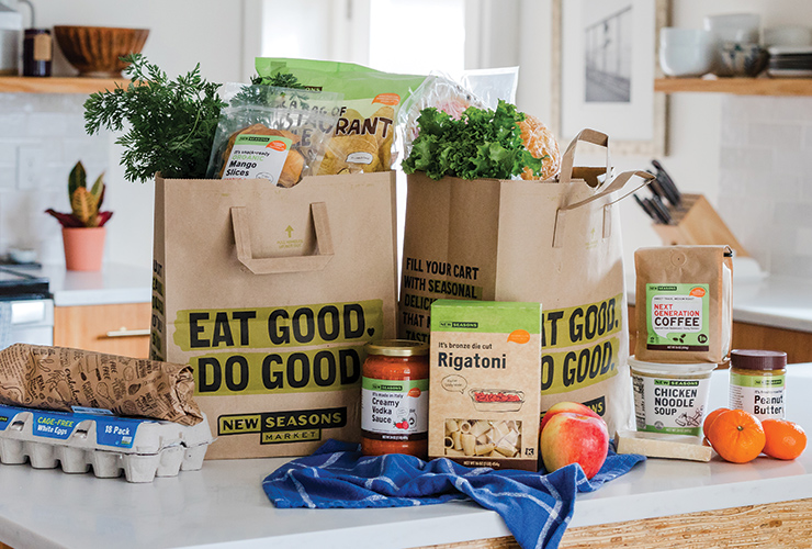 A kitchen countertop with New Seasons brown paper grocery bags filled with food.