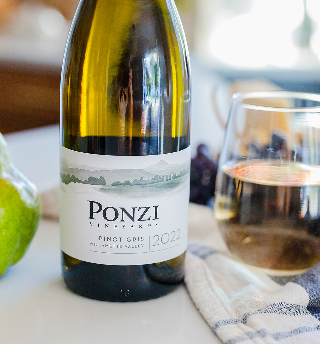 A cropped image of a bottle of white wine from Ponzi Vineyards on a tabletop next to a class of wine.