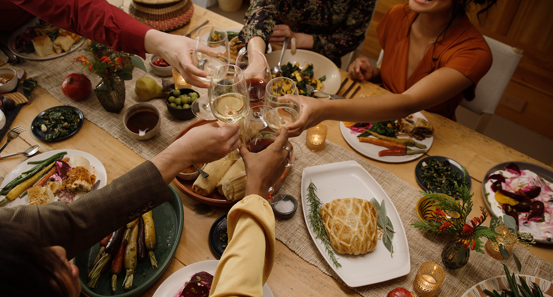 A video still featuring a celebratory holiday meal with friends and family sitting around a table toasting wine classed center table.