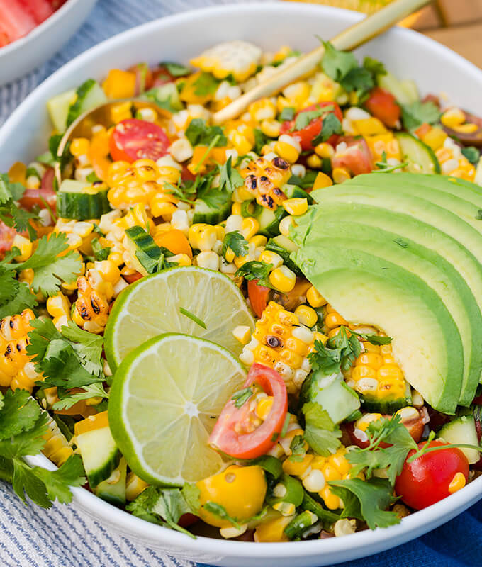 a picture of a grilled corn salad in a bowl with cilantro, sliced avocado and limes.