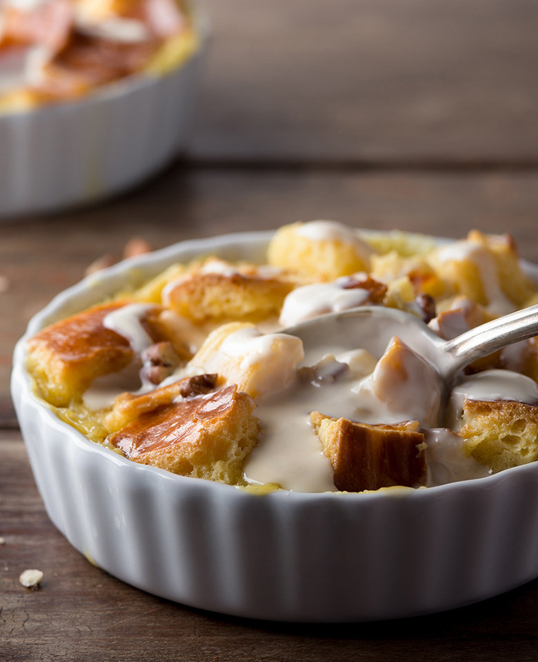 A ceramic baking pan filled with cubed bread pudding topped with a white vanilla caramel sauce.
