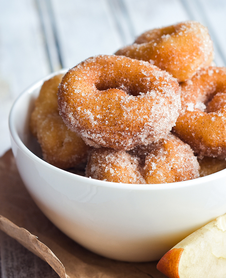 An image featuring a bowl filled with small apple cider doughnuts dusted in sugar. 