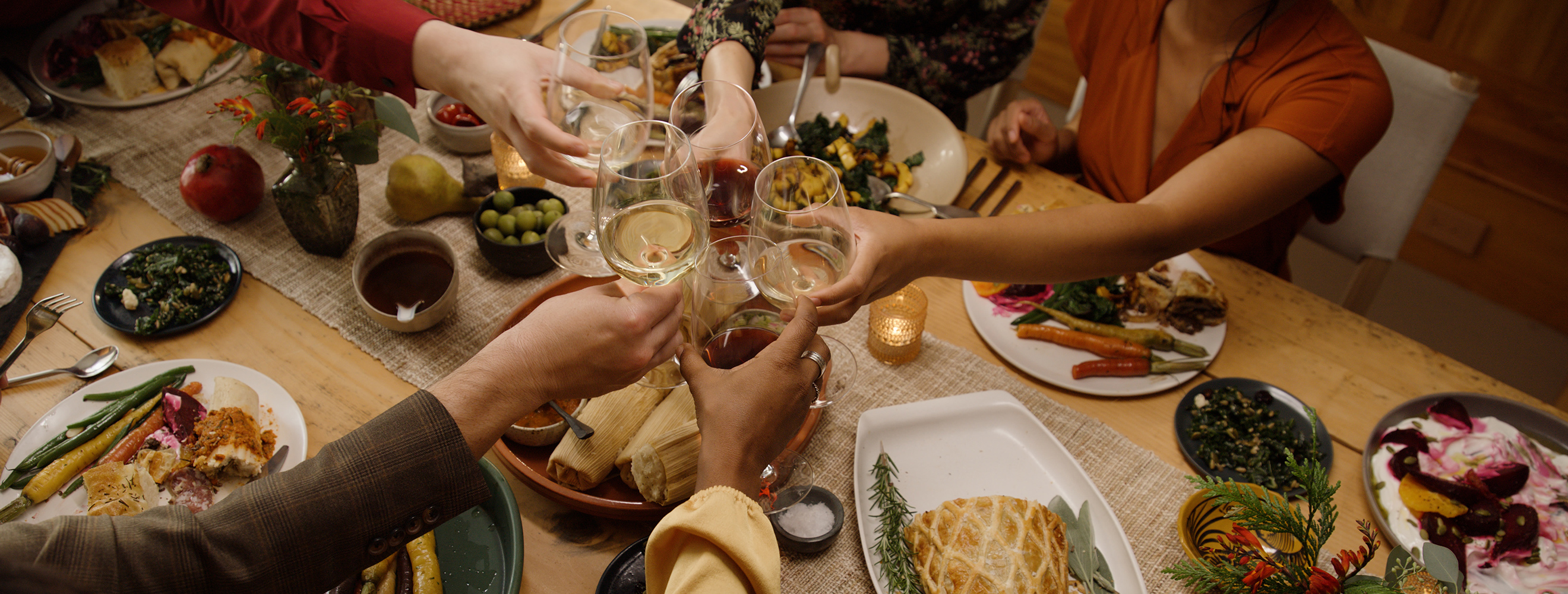 A celebratory holiday meal with friends and family sitting around a table toasting wine classed center table. 