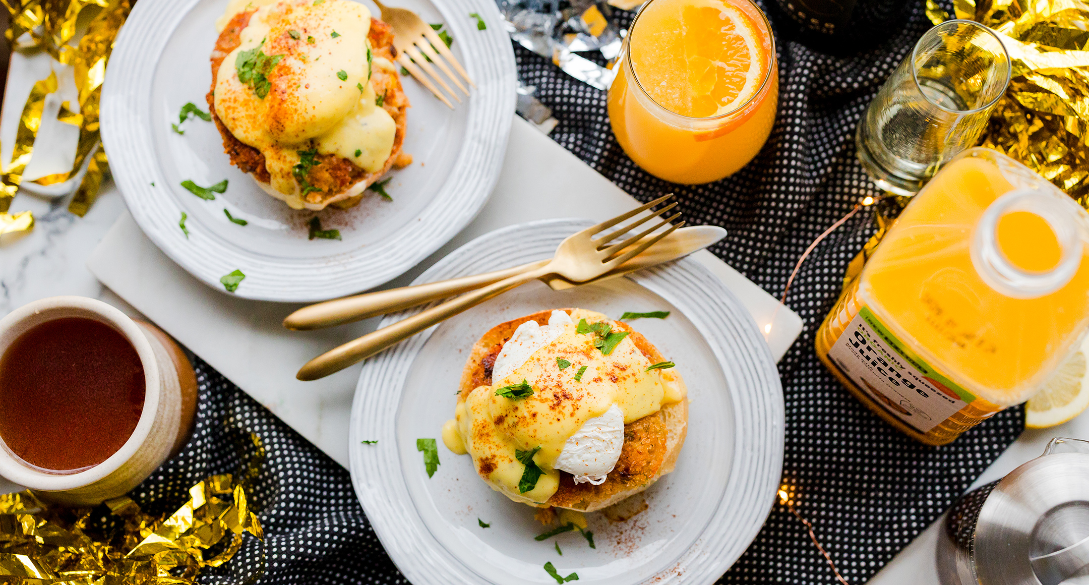 A plate topped with crab eggs Benedict slathered in Hollandaise sauce and a glass filled with mimosa on the side.
