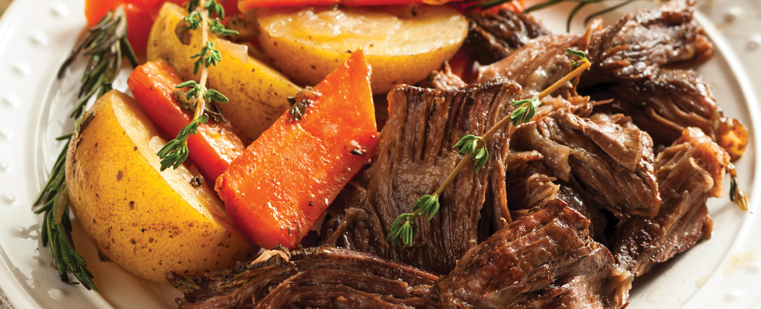 An image of cut up chuck roast with roasted carrots and potatoes