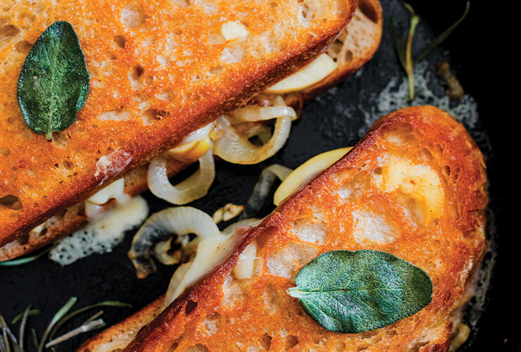 A grilled cheese sandwich with New Seasons Oregon Coast Cheddar, apple, caramelized onion, and crispy fried sage.