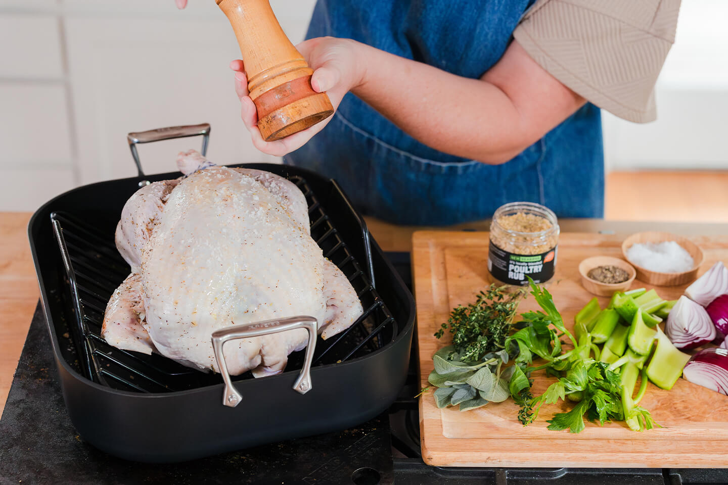 a raw turkey in a roasting pan with a person grinding fresh cracked pepper on it.