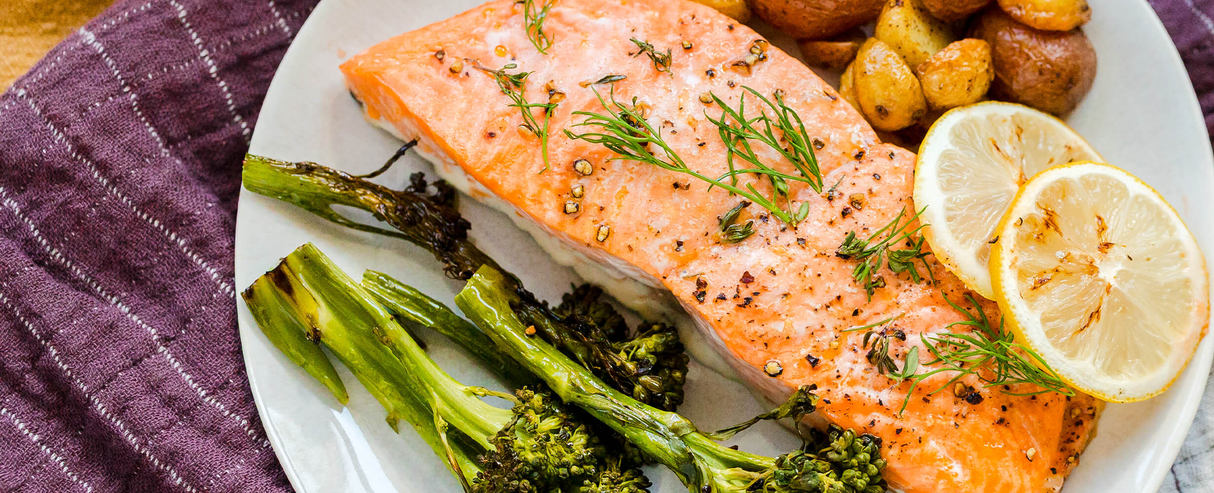 An image of a cooked coho fillet on a plate with broccolini and lemon slices. 