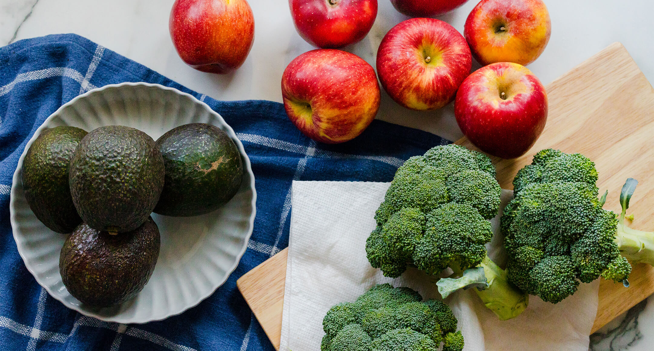 Fresh broccoli, apples, and avocados on a table.