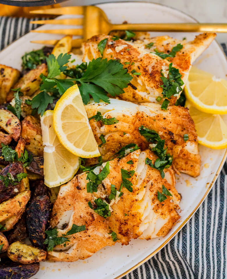 A large plate filled with garlic lemon cod, lemon wedges and roasted potatoes