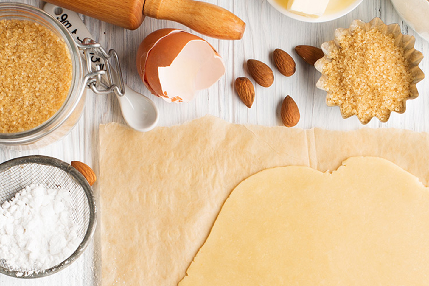 dough ready for baking on a counter freshly rolled out with eggshell, sugar, flour, rolling pine, and almonds.