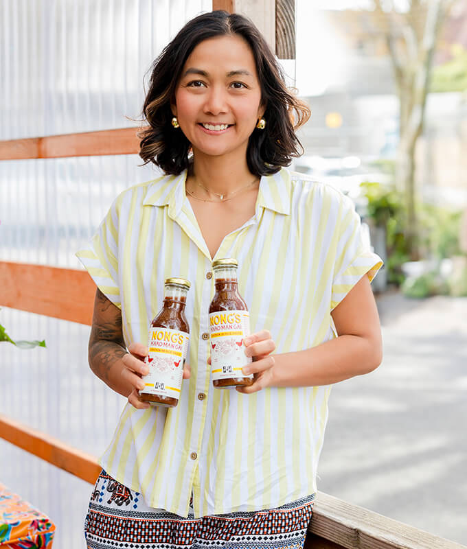 a picture of a smiling women holding two bottles of Nong's Khao Man Gai sauce.