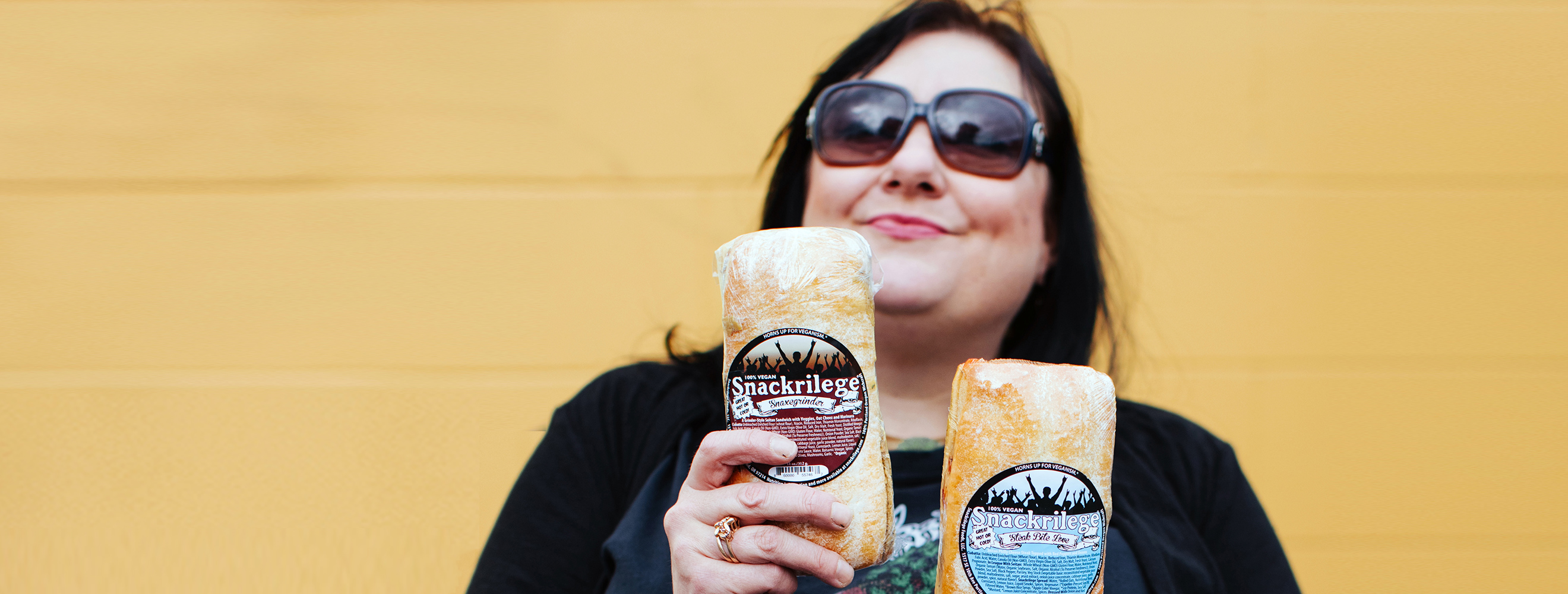 Woman wearing sunglasses against orange background holding 2 paletas