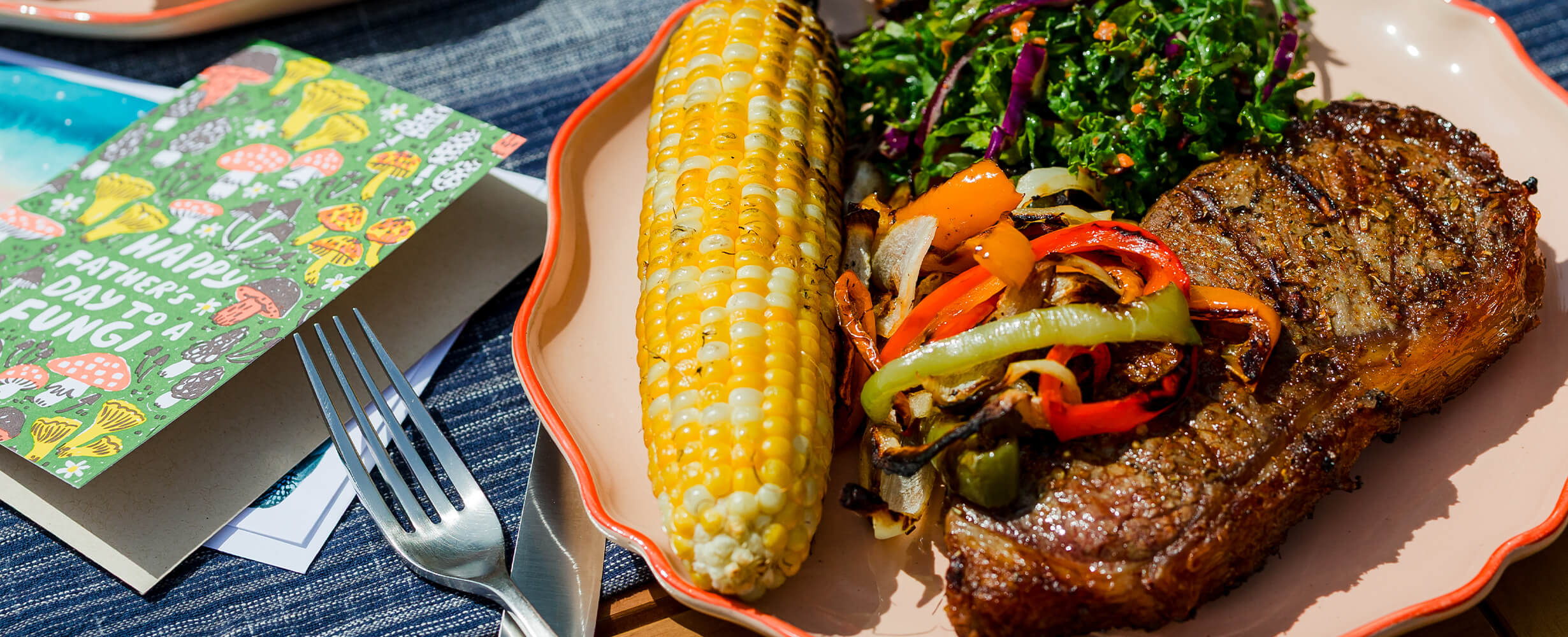 A cooked steak with grilled veggies, corn, and a salad. 
