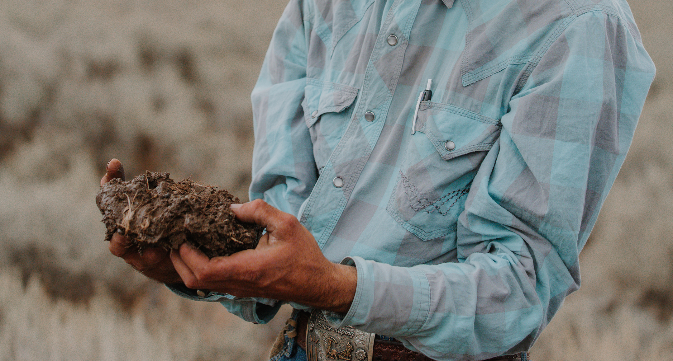 A close-up of a rancher holding a lard clod of mud. 