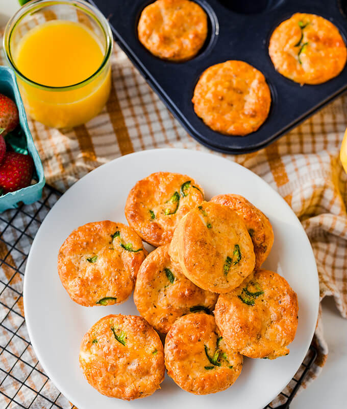 egg bites on a platter and in muffin tins with a glass of orange juice in a breakfast table scene