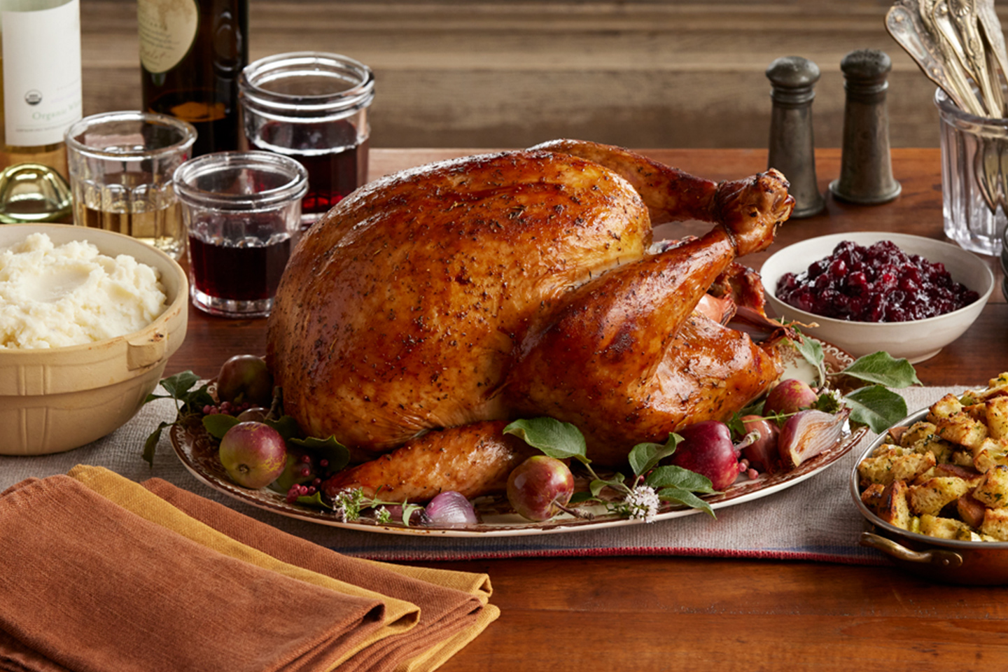 A holiday table with roasted turkey on a serving platter with cranberry sauce, bread stuffing, and mashed potatoes on the side.