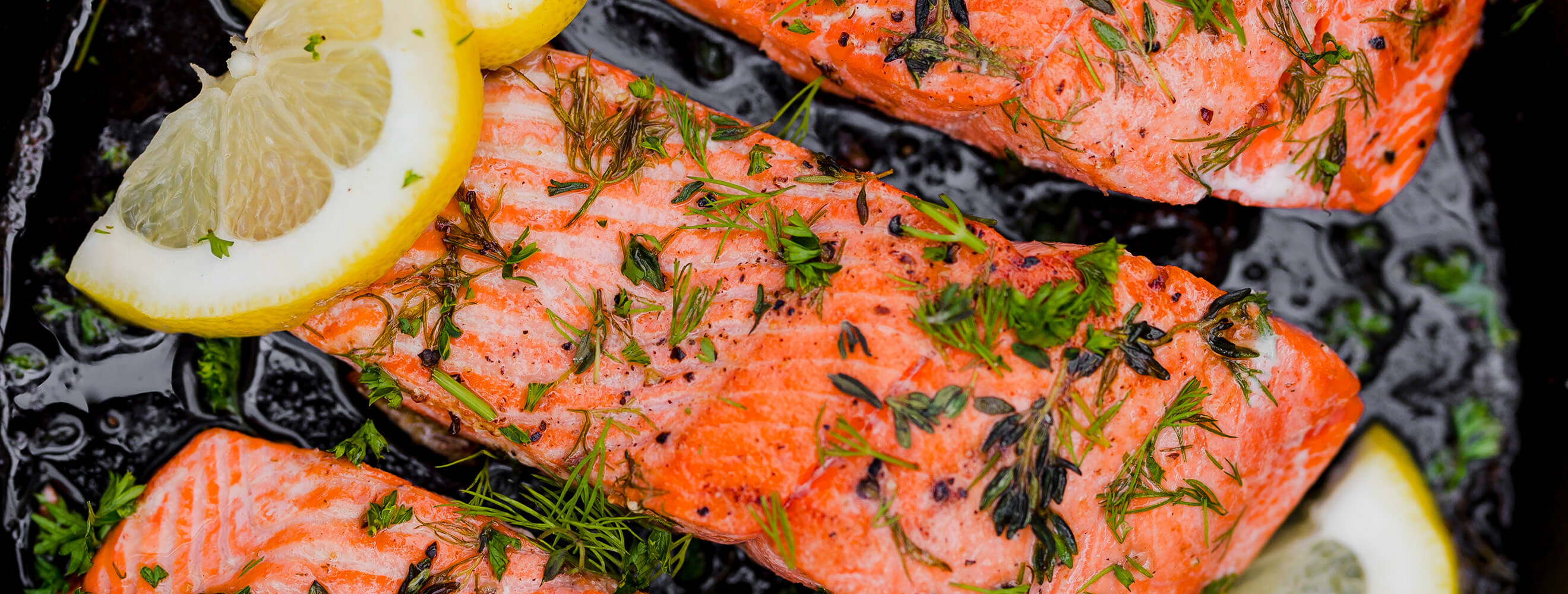 cooked filets of salmon on a grill topped with herbs and slices of lemon.