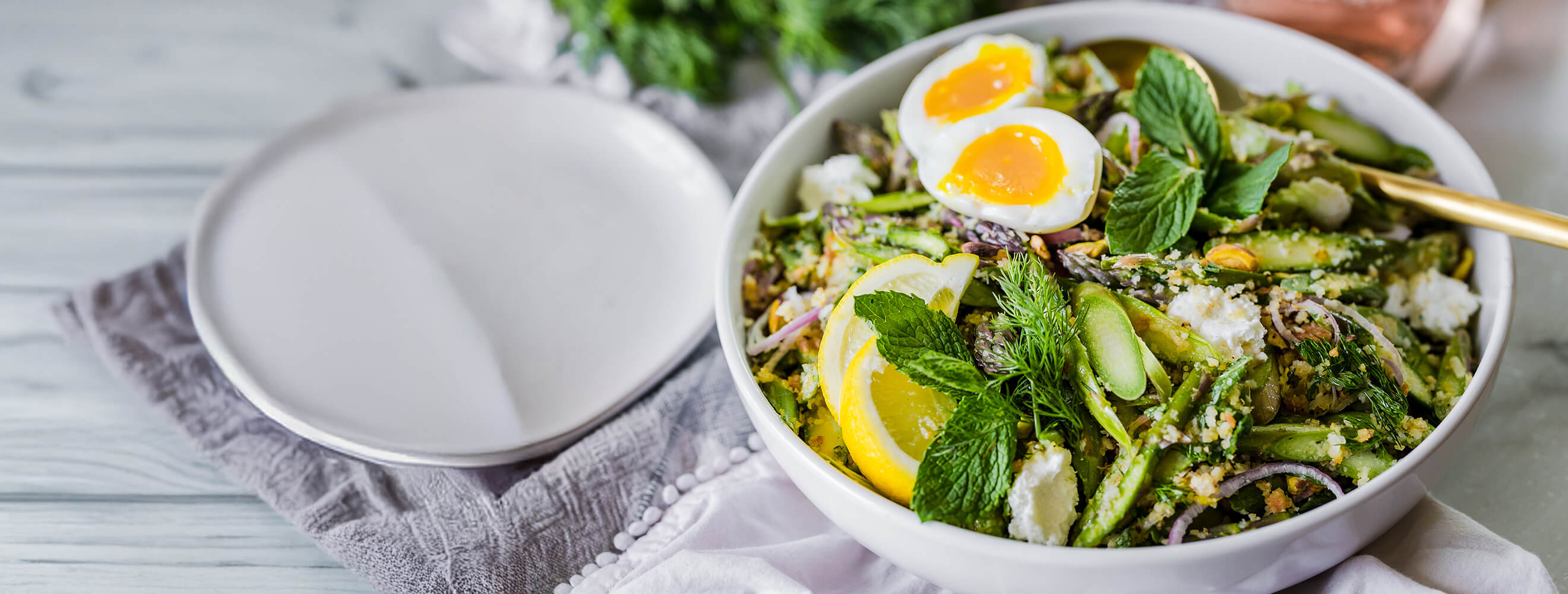a bowl of asparagus salad topped with a jammy egg and lemon wedge