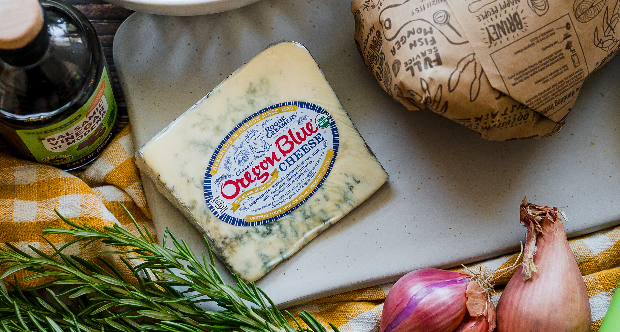 A cutting board featuring sliced salami, green olives, and Face Rock Creamery Aged Cheddar.