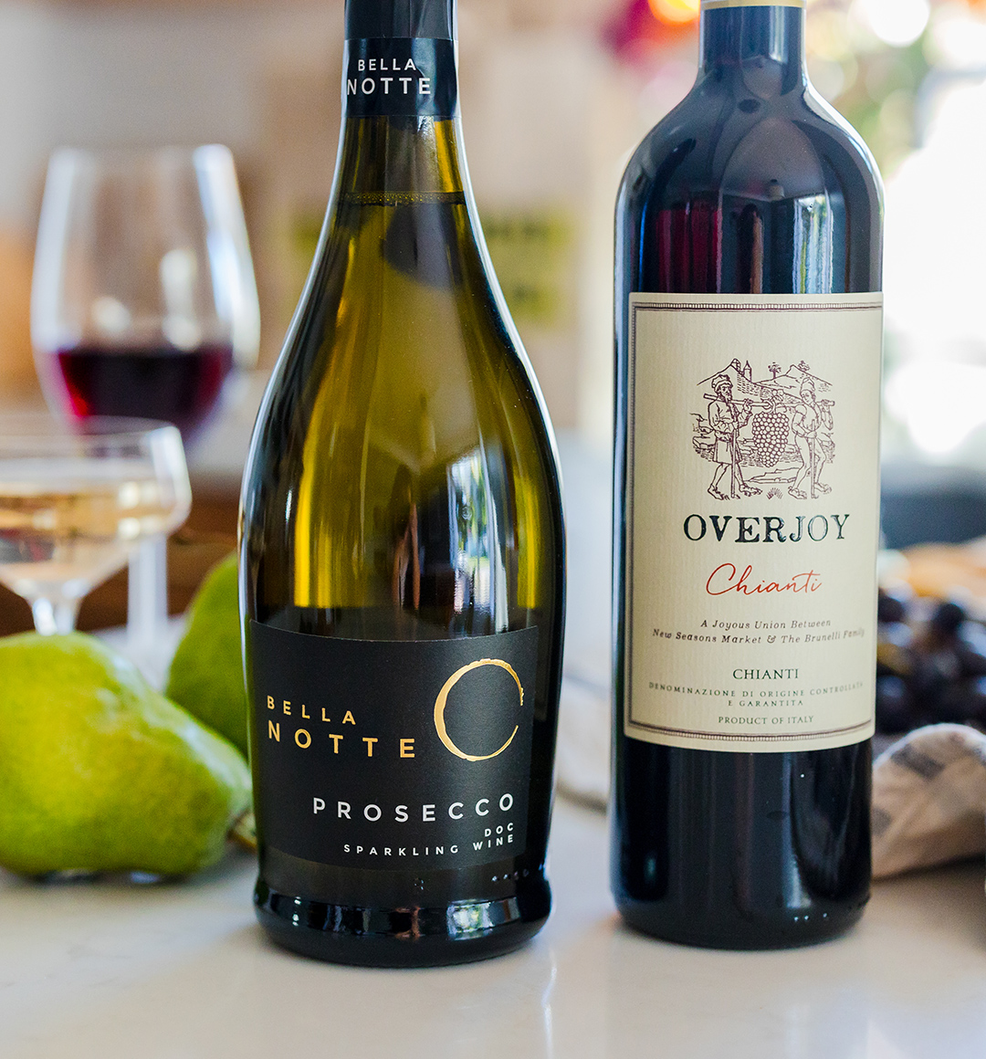 A bottle of red wine next to a bottle of white wine on a table with filled wine glasses in the background.