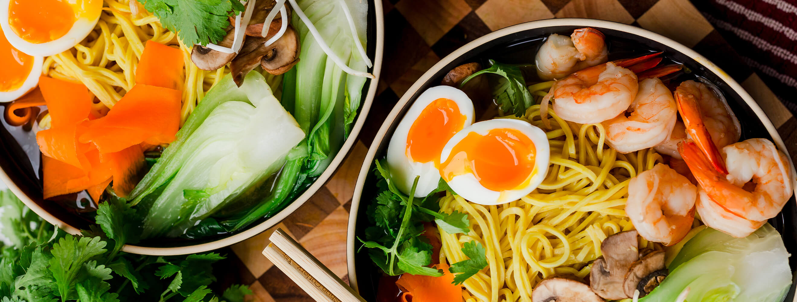 bowls of ramen topped with soft boiled egg, shrimp, carrot and bok choy