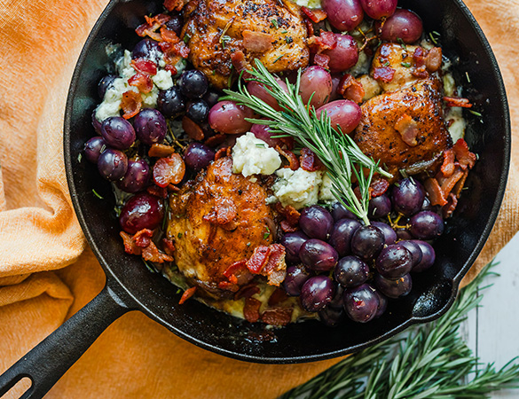 a cast iron grill with chicken, grapes and rosemary.