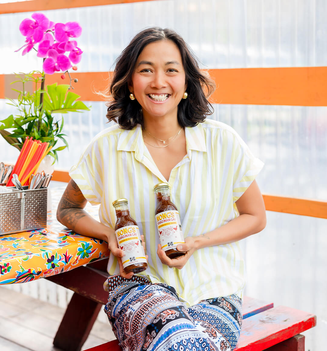 Portland restauranteur Nong Poonsukwattana holding two bottles of her Khao Man Gai Sauce.