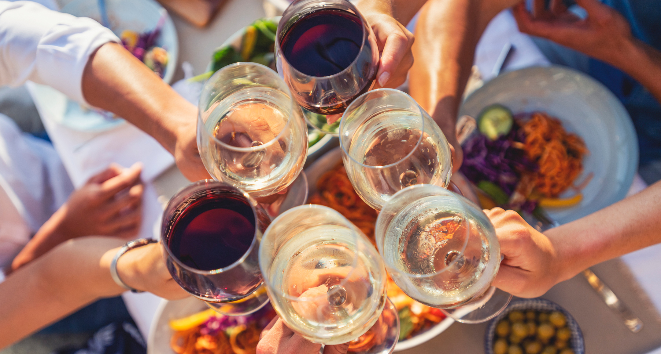 People toast wine glasses filled with red and white wines.