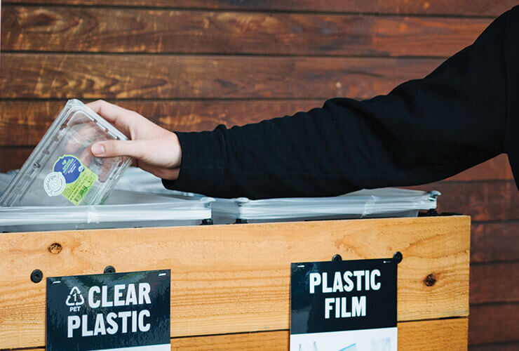 An image showing an individual placing an empty plastic container in a designated recycling bin.