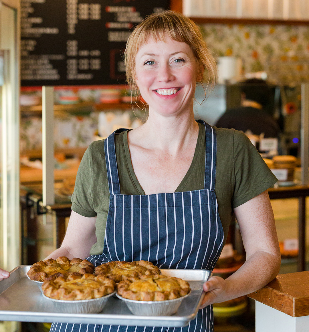 Kate McMillen, owner of Lauretta Jean’s, holding a sheet pan with four savory pot pies. 