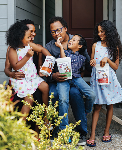 Jovani Prince of The Cracker King with 3 children holding bags of Cracker King snacks