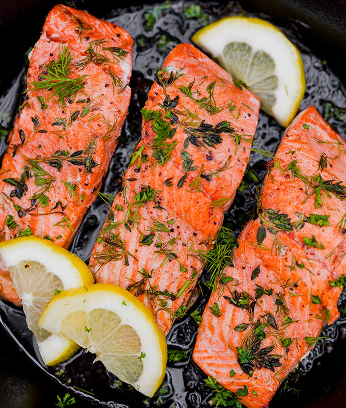 filets of salmon on a grill with herbs and sliced lemon