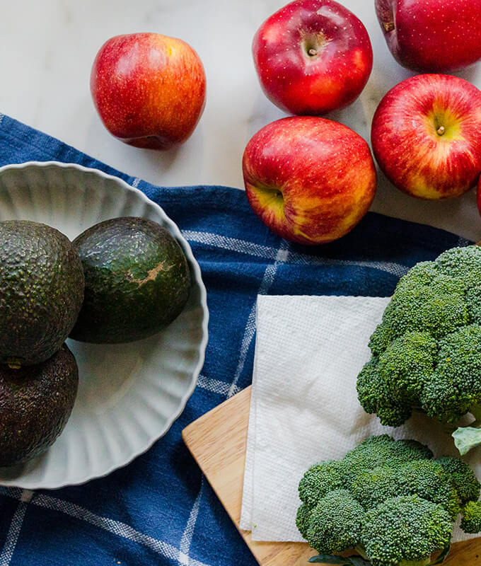 fresh fruit and vegetables like apples, broccoli and avocados on a table