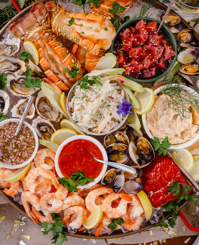 A sea-cuterie board featuring an array of seafood on ice, including shrimp, lobster tails and smoked fish.