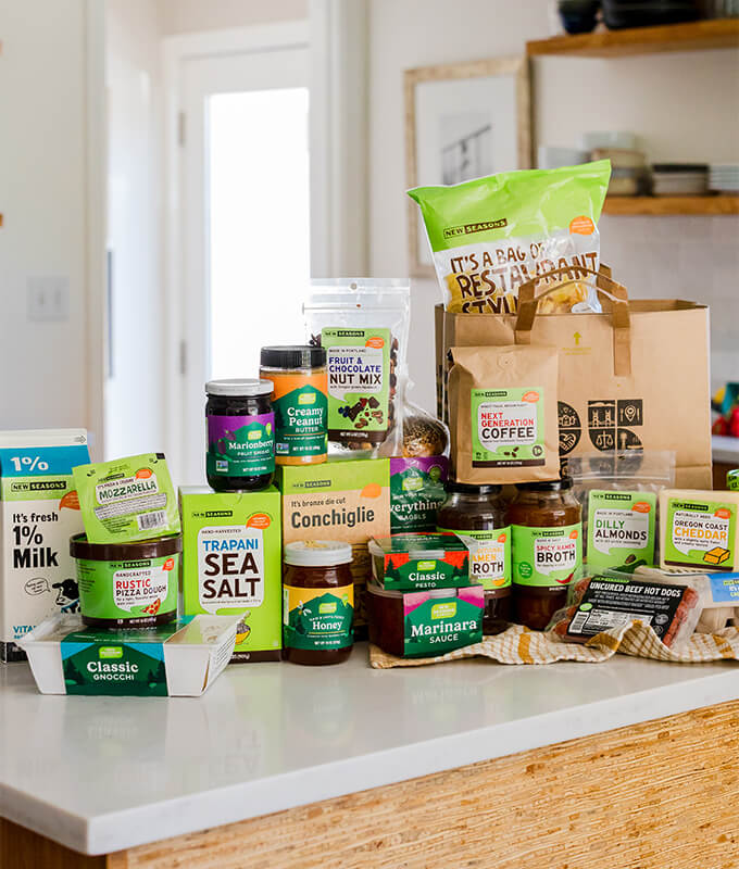 New Seasons branded packaged grocery items on a kitchen counter including pasta, ice cream, salt, nut butters, chips and more.