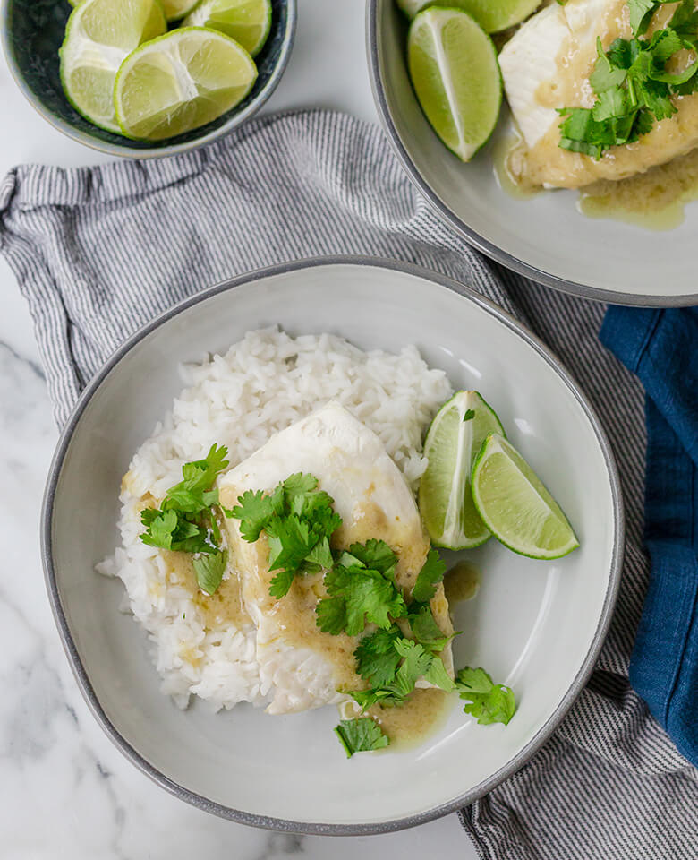 Aromatic Coconut Milk Poached Halibut served on a plate with lime wedges and rice.