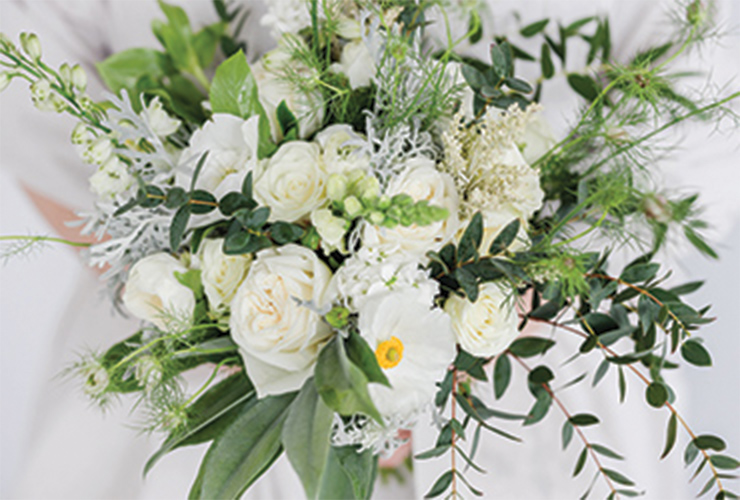 A bouquet of white roses with poppies and sprigs of green plants.