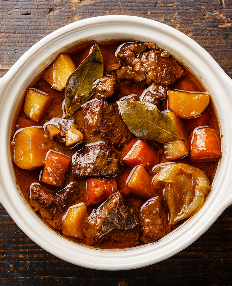 A pot of beef stew with chopped potatoes, carrots, and onion with bay leaves. 