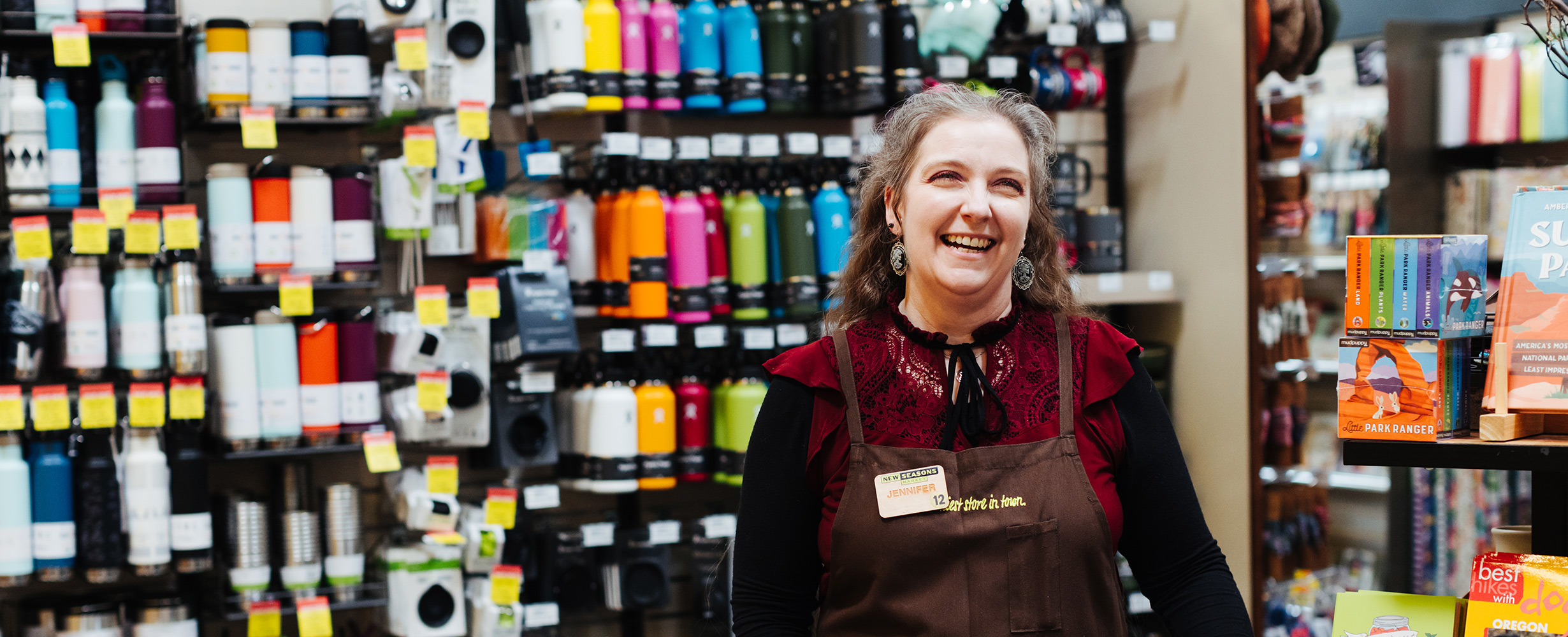 Smiling New Seasons staff member in front of merchandise shelves