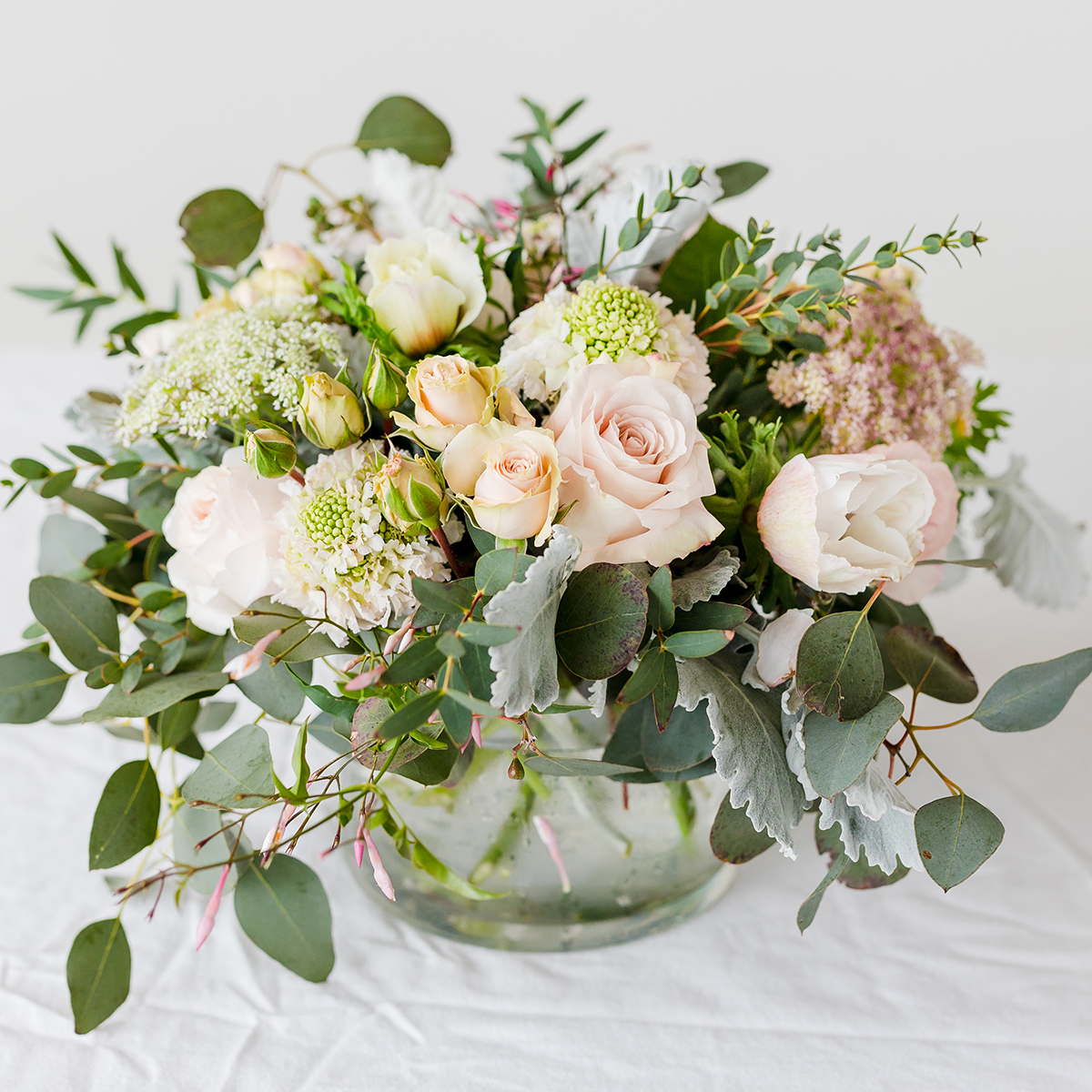 blush and white flowers and greenery in a glass bowl