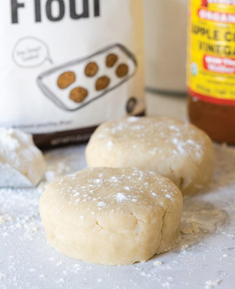 Showing a kitchen work surface with two balls of pie dough dusted with flour. 