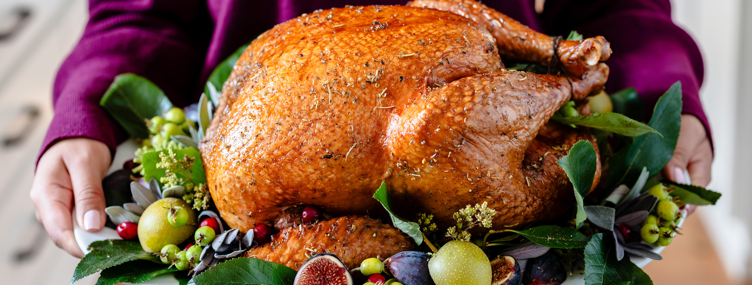 a person in a purple sweater holding a beautiful roasted thanksgiving turkey