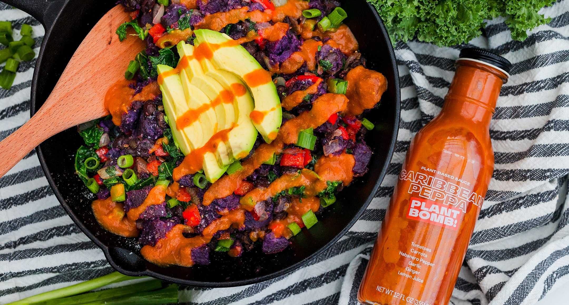 bowl of sweet potato hash topped with avocado next to a bottle of Plant Bomb sauce