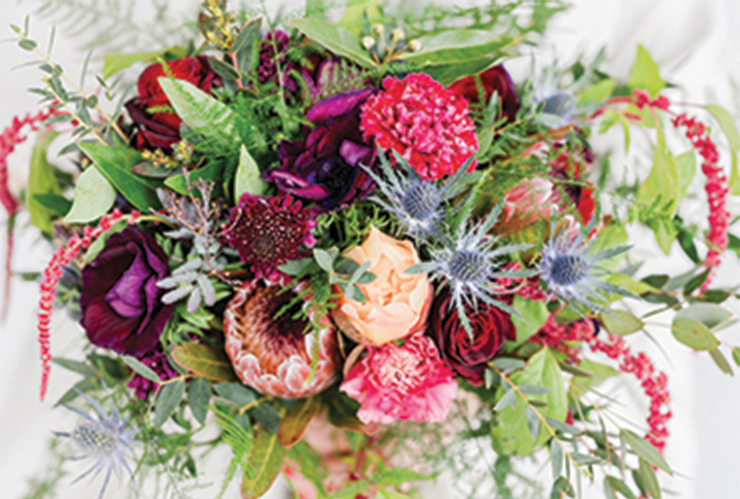 A big, overflowing bouquet of red, purple, and pink flowers interspersed with green stems.