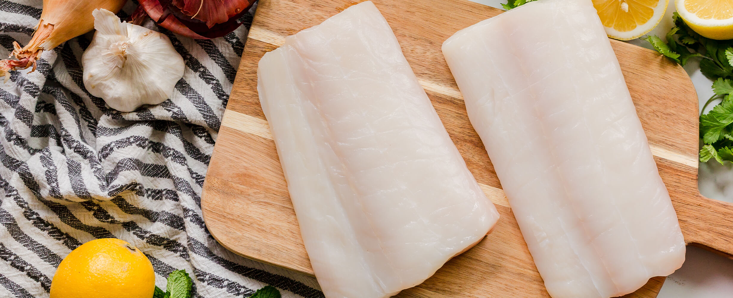 A top down image of 2 halibut fillets on a wood cutting board.
