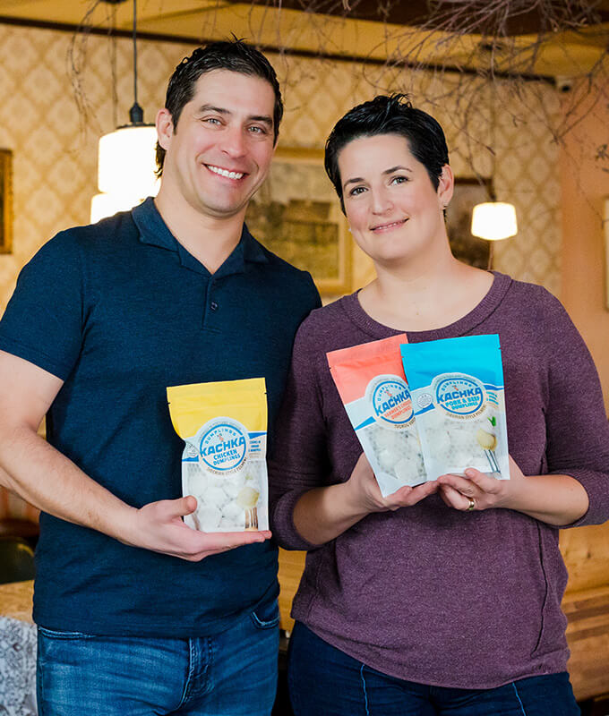 two smiling people holding packages of Kachka frozen dumplings.
