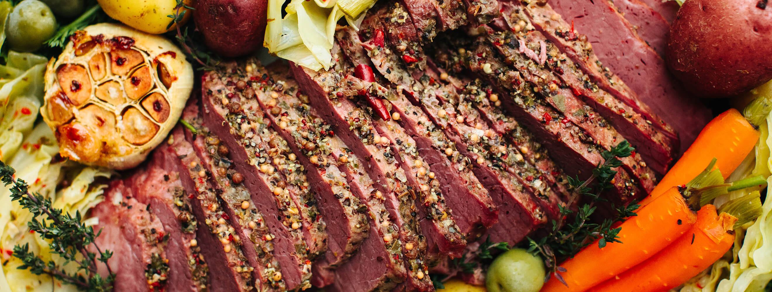 a close up of sliced corned beef with garlic, carrots, cabbage, and potatoes.