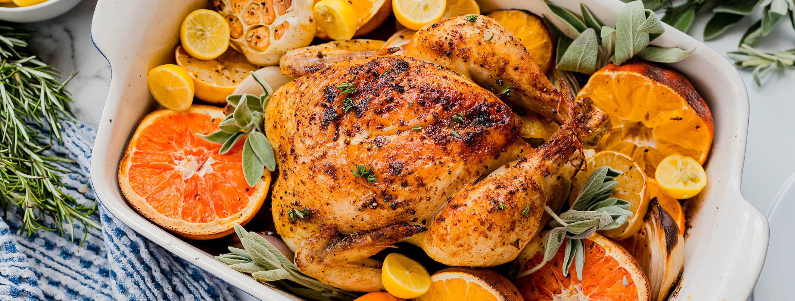 a casserole dish with roasted chicken surrounded by citrus, garlic, onion and herbs