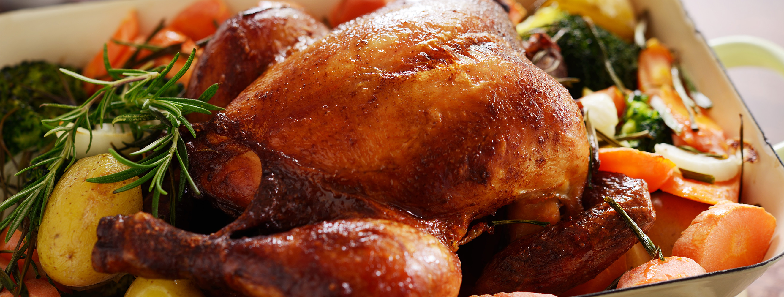 Freshly roasted whole chicken in a casserole dish with vegetables.